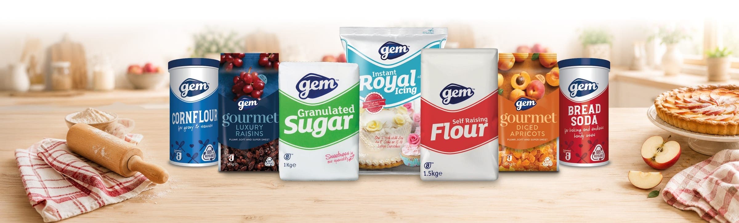 Gem baking products lineup including cornflour, luxury raisins, granulated sugar, instant royal icing, self raising flour, diced apricots, and bread soda on a kitchen counter